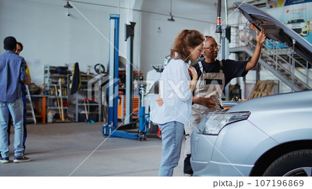 Certified technician in garage workspace fixing car for customer, thoroughly checking underneath vehicle hood. Specialist doing annual maintenance on client automobile in auto repair shop Certified technician in garage workspace fixing car for customer, thoroughly checking underneath vehicle hood. Specialist doing annual maintenance on client automobile in auto repair shop 107196869