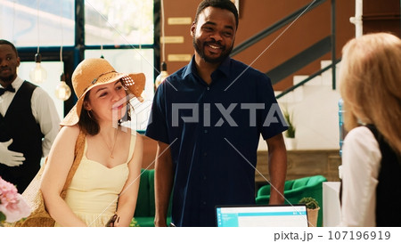 Couple giving access room card to receptionist at front desk, leaving summer tropical resort. Tourists doing checkout process and handing key to hotel concierge, saying goodbye. 107196919