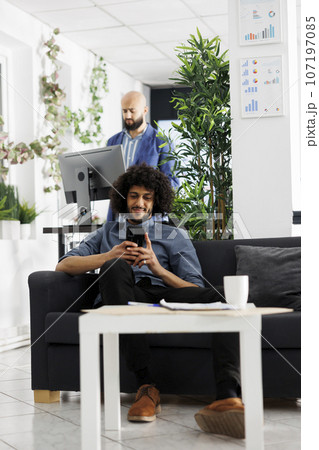 Smiling start up business entrepreneur typing message on smartphone in office. Young man executive manager chatting in social media on mobile phone while realxing at workplace 107197085