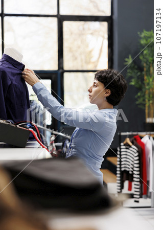 Clothing store worker arranging formal shirt on mannequin, preparing boutique for customers. Caucasian woman with short hair working with fashionable merchandise in shopping mall Clothing store worker arranging formal shirt on mannequin, preparing boutique for customers. Caucasian woman with short hair working with fashionable merchandise in shopping mall 107197134
