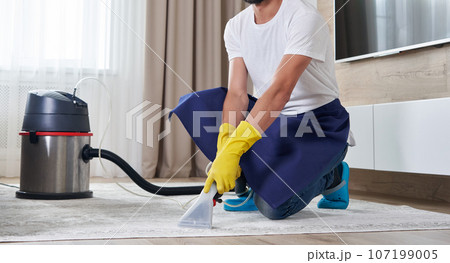 Man Cleaning Carpet In The Living Room Using Vacuum Cleaner At Home. Cleaning service concept 107199005