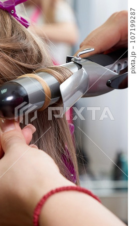 Hairdresser makes hairstyle girl with long hair in a beauty salon. Create curls with curling irons 107199287