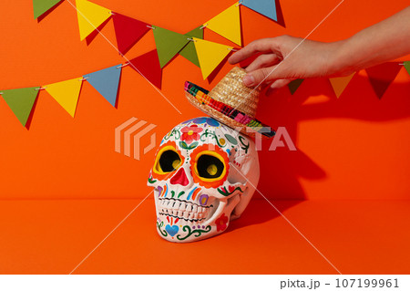 Mexican skull and sombrero in female hand on orange background Mexican skull and sombrero in female hand on orange background 107199961