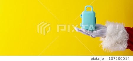 Toy suitcase on Santa's hand on yellow background, space for text Toy suitcase on Santa's hand on yellow background, space for text 107200014