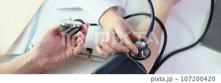 Doctor measures patient's blood pressure using sphygmomanometer and stethoscope. 107200420