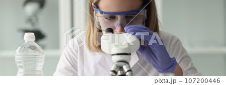 Female scientist in glasses looking at test samples through microscope. Female scientist in glasses looking at test samples through microscope. 107200446