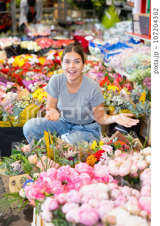 Cheerful girl choosing floral arrangement amidst flower market stalls Cheerful girl choosing floral arrangement amidst flower market stalls 107204382