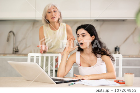 Elderly woman quarrels with young woman working at laptop 107204955
