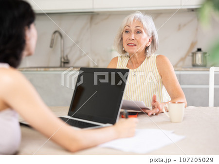 Mature woman consulting with female real estate agent in home 107205029