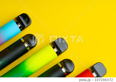 Colorful disposable electronic cigarettes on yellow background 107206372