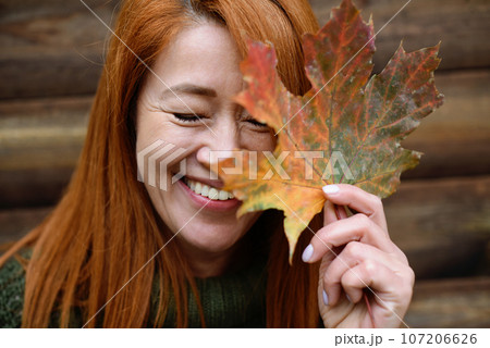 Laughing red-haired middle-aged woman, closed eyes and maple leaf 107206626