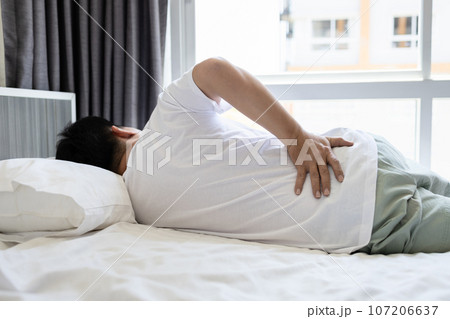 Stressed asian man having a backache,sore hips,waist hurts,unhappy adult people suffering from low lumbar pain or acute back strain,lying on the mattress at home,health care,medical,lifestyle concept Stressed asian man having a backache,sore hips,waist hurts,unhappy adult people suffering from low lumbar pain or acute back strain,lying on the mattress at home,health care,medical,lifestyle concept 107206637