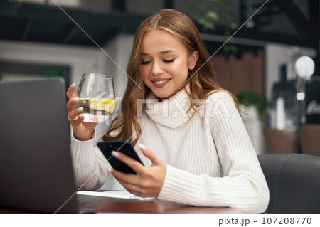 Beautiful woman sitting at the table and holding glass of water. Online job. Girl Working at cafe 107208770