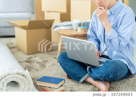 パソコンを見ながら引越しの荷造りをする若い男性のボディパーツ パソコンを見ながら引越しの荷造りをする若い男性のボディパーツ 107209003