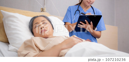 Asian nurse check saline and check patient elderly while asleep on bed at hospital ward. 107210236
