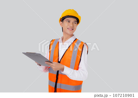 Portrait young asian engineer man wearing helmet looking document or report on clipboard isolated. 107210901