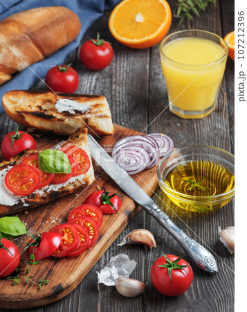 Fresh sandwiches baguette , tomatoes, vegetables and olive oil, ingredients for making a vegan sandwich, close-up. Freshly squeezed orange juice in a glass Dark wooden background Fresh sandwiches baguette , tomatoes, vegetables and olive oil, ingredients for making a vegan sandwich, close-up. Freshly squeezed orange juice in a glass Dark wooden background 107212396