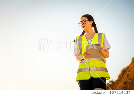 Inspection environmentalist. Bottom view of volunteer woman wearing vest and using pad for analyzing water. In background is sky. Copy space. Concept of air pollution and ecology Inspection environmentalist. Bottom view of volunteer woman wearing vest and using pad for analyzing water. In background is sky. Copy space. Concept of air pollution and ecology 107214334