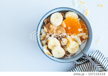 Multigrain wholewheat breakfast cereals with tangerine, coconut chips, peanut butter and banana, top view. 107216328