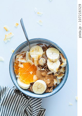 Multigrain wholewheat breakfast cereals with tangerine, coconut chips, peanut butter and banana, top view. 107216329