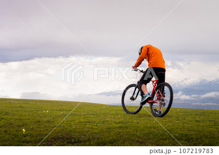 Professional mountain biker on the background of mountains and green hills. Tired mtb rider in full face helmet outdoors 107219783
