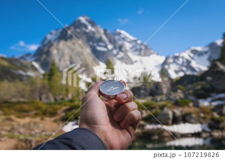 Snow-capped mountains and a tourist hand with an old metal compass in the foreground. Nature reserve, landscape photography 107219826