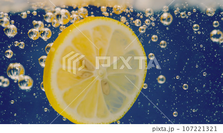 Underwater of freshly squeezed sweetened lemonade which raw lemons slice falling in soda water against dark blue or black background. Close up lemonade or Highball lemon cocktail cold refreshing drink 107221321