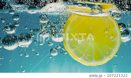 Underwater of freshly squeezed sweetened lemonade which raw lemons slice falling in soda water against dark blue or black background. Close up lemonade or Highball lemon cocktail cold refreshing drink 107221322