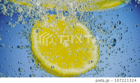 Underwater of freshly squeezed sweetened lemonade which raw lemons slice falling in soda water against dark blue or black background. Close up lemonade or Highball lemon cocktail cold refreshing drink 107221324
