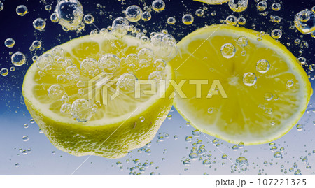 Underwater of freshly squeezed sweetened lemonade which raw lemons slice falling in soda water against dark blue or black background. Close up lemonade or Highball lemon cocktail cold refreshing drink 107221325