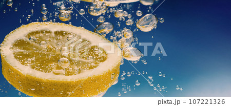 Underwater of freshly squeezed sweetened lemonade which raw lemons slice falling in soda water against dark blue or black background. Close up lemonade or Highball lemon cocktail cold refreshing drink 107221326
