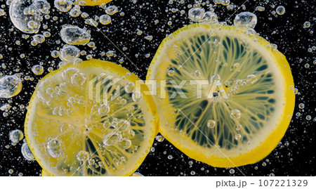 Underwater of freshly squeezed sweetened lemonade which raw lemons slice falling in soda water against dark blue or black background. Close up lemonade or Highball lemon cocktail cold refreshing drink 107221329