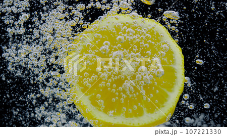 Underwater of freshly squeezed sweetened lemonade which raw lemons slice falling in soda water against dark blue or black background. Close up lemonade or Highball lemon cocktail cold refreshing drink 107221330
