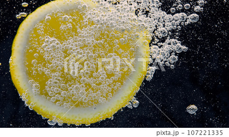 Underwater of freshly squeezed sweetened lemonade which raw lemons slice falling in soda water against dark blue or black background. Close up lemonade or Highball lemon cocktail cold refreshing drink 107221335
