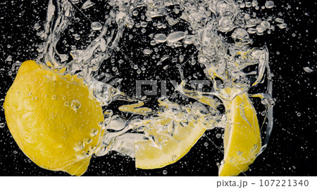 Underwater of freshly squeezed sweetened lemonade which raw lemons slice falling in soda water against dark blue or black background. Close up lemonade or Highball lemon cocktail cold refreshing drink 107221340