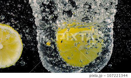Underwater of freshly squeezed sweetened lemonade which raw lemons slice falling in soda water against dark blue or black background. Close up lemonade or Highball lemon cocktail cold refreshing drink 107221344