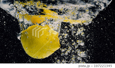Underwater of freshly squeezed sweetened lemonade which raw lemons slice falling in soda water against dark blue or black background. Close up lemonade or Highball lemon cocktail cold refreshing drink 107221345