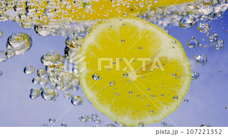 Underwater of freshly squeezed sweetened lemonade which raw lemons slice falling in soda water against dark blue or black background. Close up lemonade or Highball lemon cocktail cold refreshing drink 107221352