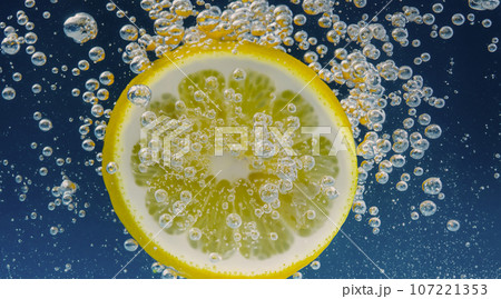 Underwater of freshly squeezed sweetened lemonade which raw lemons slice falling in soda water against dark blue or black background. Close up lemonade or Highball lemon cocktail cold refreshing drink 107221353
