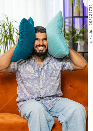 Neighbors repair work, irritated man by loud music at home cover ears with pillows annoyed by noise 107223754