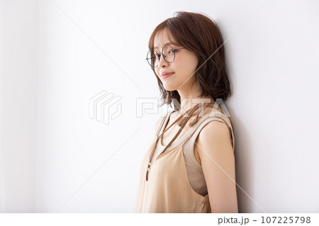 白壁に寄りかかるメガネをかけた女子大生 107225798