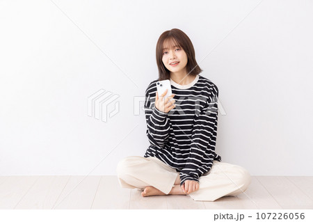 床に座りスマートフォンを使う若い女性 107226056