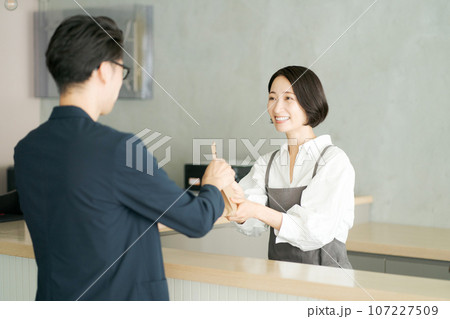 商品を受け渡すカフェ店員と客 107227509