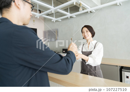 商品を受け渡すカフェ店員と客 107227510