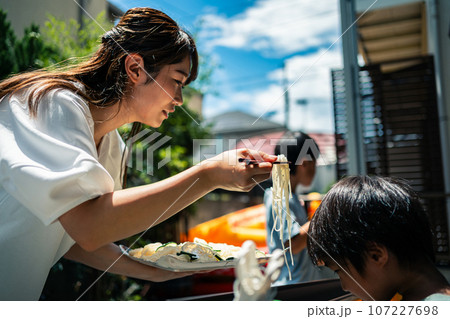 お庭で雨どい流しそうめんをする家族 107227698