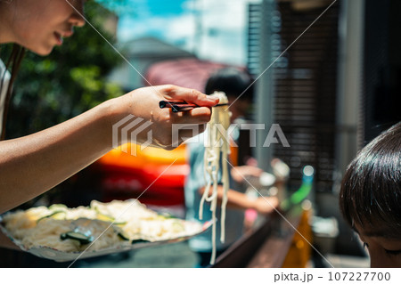 お庭で雨どい流しそうめんをする家族 107227700