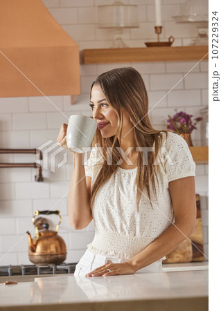 Woman drinking from mug in kitchen 107229324