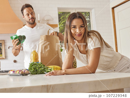 Smiling couple with paper shopping bag and groceries in kitchen 107229348