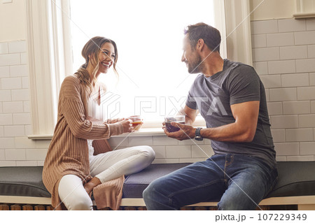 Smiling couple relaxing by window at home Smiling couple relaxing by window at home 107229349