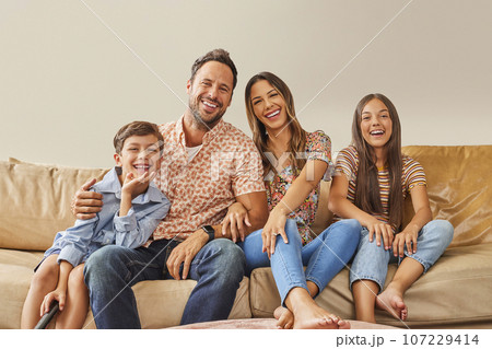Portrait of smiling family with two children (8-9, 12-13) watching TV on sofa 107229414